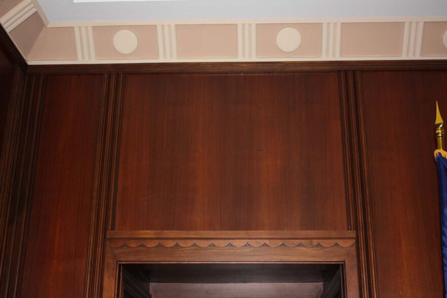 Fluted wall wood paneling and scalloped detail over door frame in Mayor’s conference room.