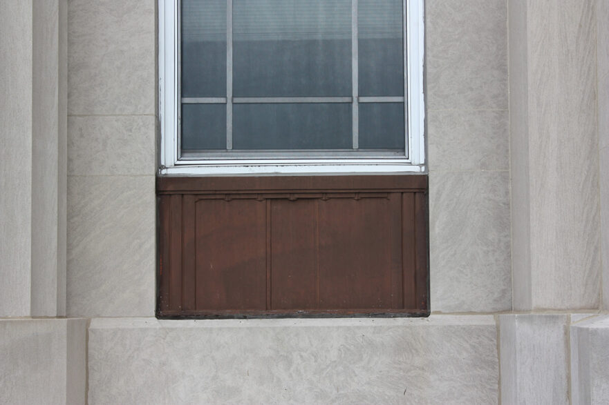 Small metal panels that are beneath the first floor windows on the west façade of City Hall, note they have minimal decorations, circa 2022.