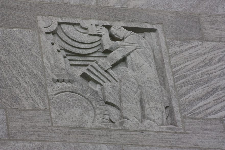 Carving on the upper area of the north and south extensions of City Hall, this is an Art Deco figure operating machinery, circa 2022.